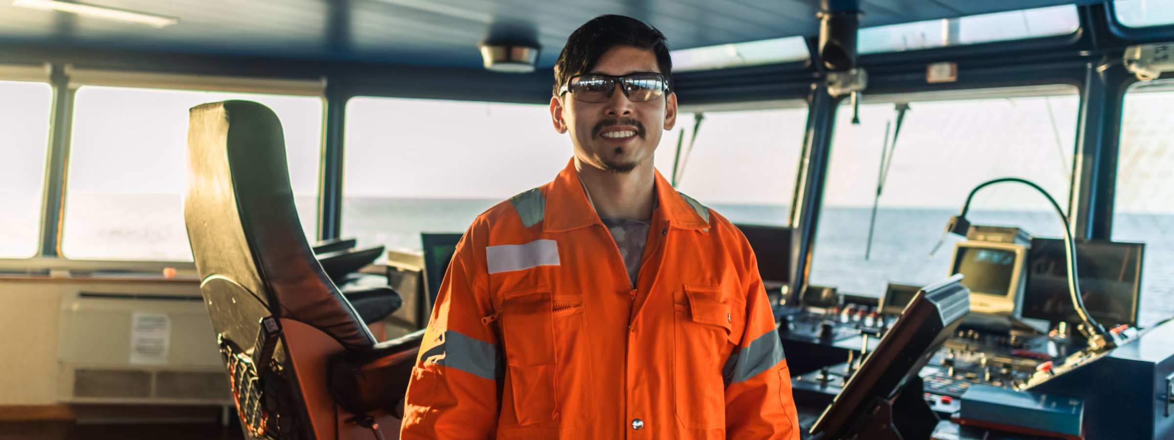 A deck officer is on the bridge of a vessel, wearing a coverall during a navigation watch at sea.