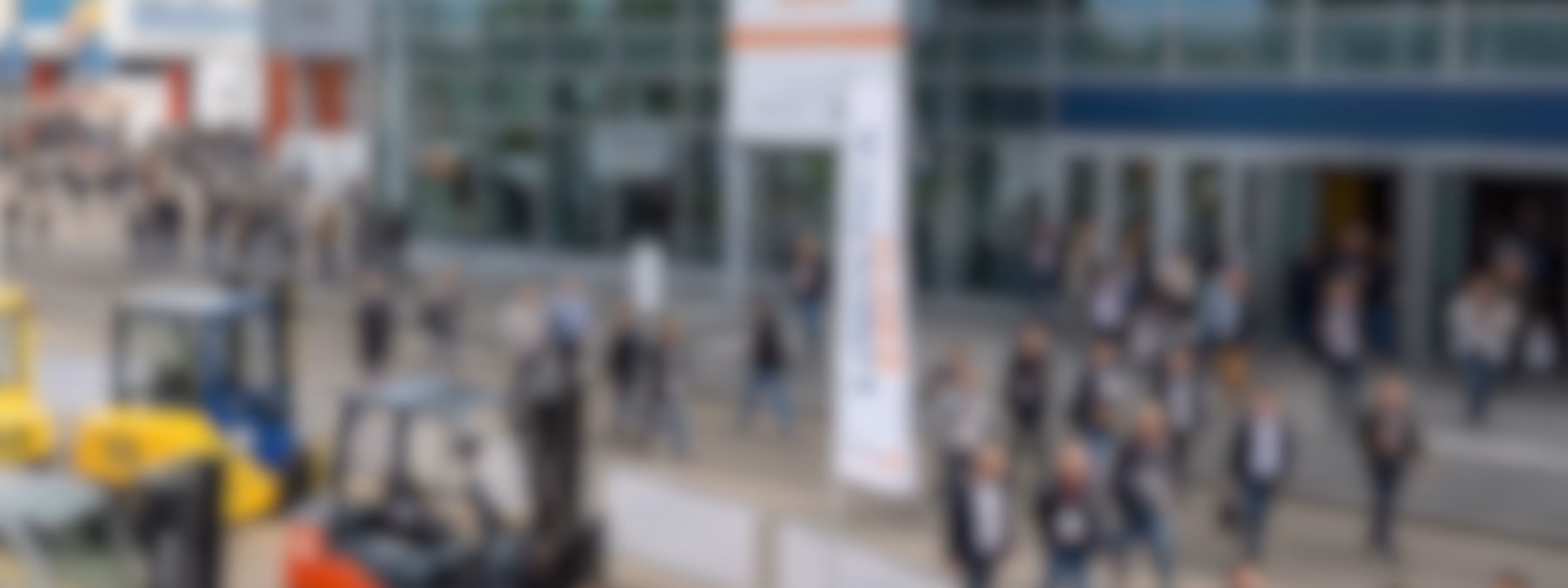 Besucher schlendern durch den Eingangsbereich einer großen Industriemesse mit Ausstellungshallen, Produktvorführungen und Gelegenheiten zum Networking, bei der Innovation, Geschäftsentwicklung, fachliche Zusammenarbeit sowie Fortschritte in den Bereichen Fertigung, Prüfung, Inspektion und Zertifizierungsdienstleistungen im Mittelpunkt stehen.