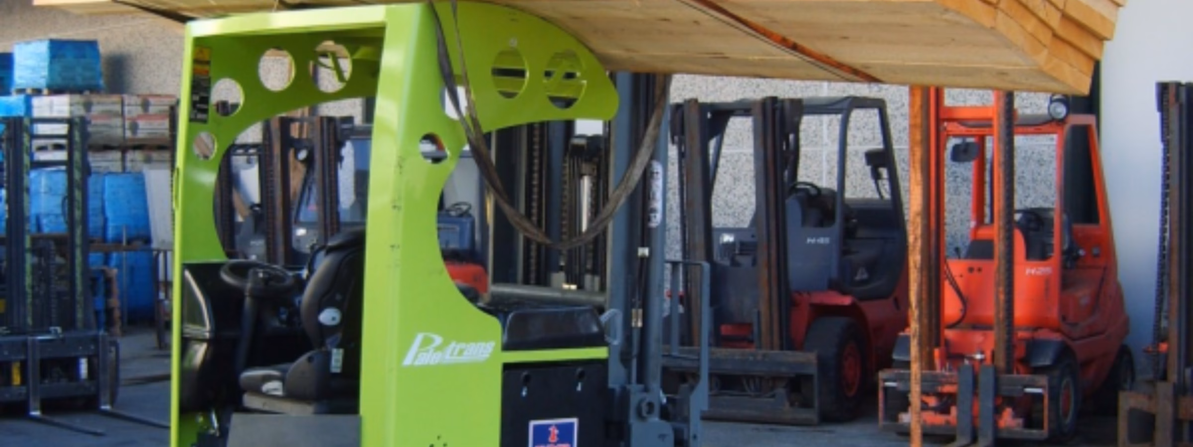 Ein Industriegabelstapler hebt und transportiert auf einem Lagerhof einen großen Stapel Holzbretter, die mit Hebegurten gesichert sind. Dabei stehen der sichere Materialumschlag, der Transport schwerer Lasten, Lagerabläufe, logistische Effizienz und qualitätskontrollierte industrielle Prozesse im Vordergrund.