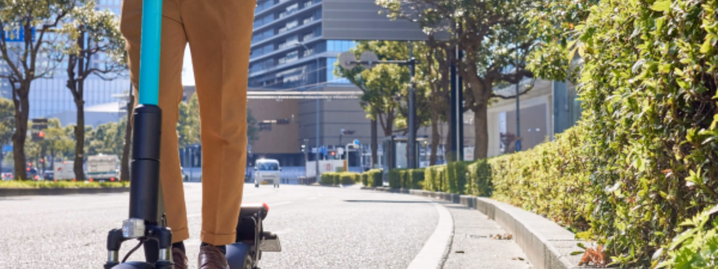 Ein E-Scooter-Fahrer fährt auf einem eigens dafür vorgesehenen städtischen Weg, umgeben von modernen Gebäuden und begrünten Anlagen, und verdeutlicht dabei die Bedeutung von Mikromobilitätslösungen, nachhaltigem Verkehr, Produktsicherheit, Einhaltung gesetzlicher Vorschriften und Innovation in städtischen Mobilitätssystemen.