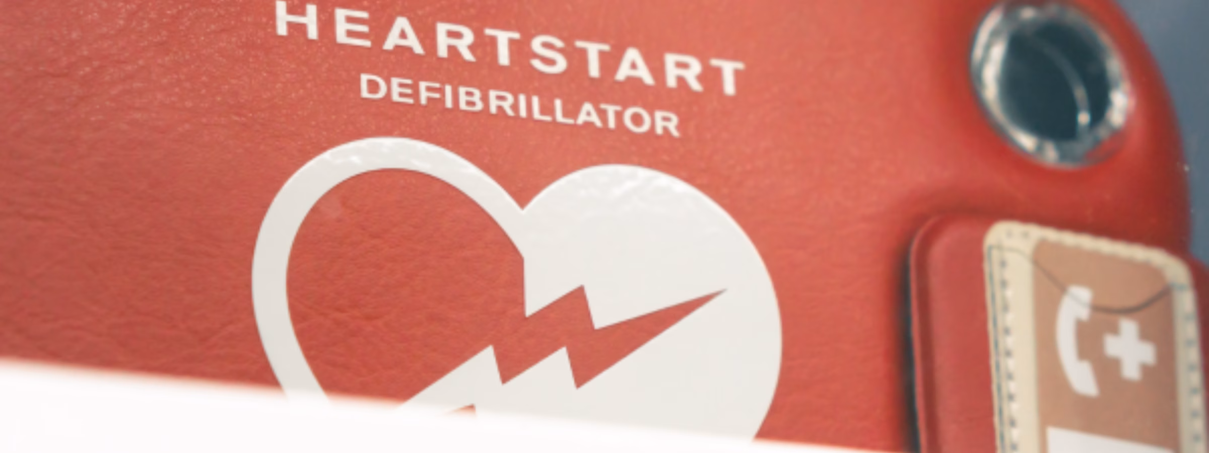 Nahaufnahme eines automatisierten externen Defibrillators (AED) mit deutlichen Notfallkennzeichnungen, die die Sicherheit am Arbeitsplatz, die Notfallvorsorge, die Erste-Hilfe-Bereitschaft und lebensrettende medizinische Geräte in professionellen Umgebungen hervorheben.