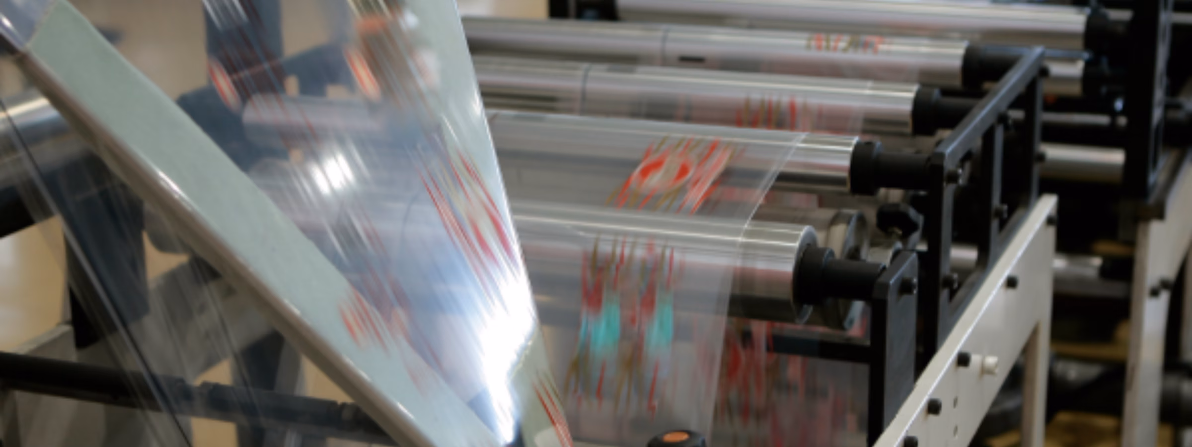 Eine transparente Verpackungsfolie durchläuft eine automatisierte Produktionslinie, die mit Walzen und Verarbeitungsmaschinen ausgestattet ist. Der Schwerpunkt liegt auf der Herstellung flexibler Verpackungen, der Qualitätskontrolle, der industriellen Fertigung und effizienten Verpackungslösungen.