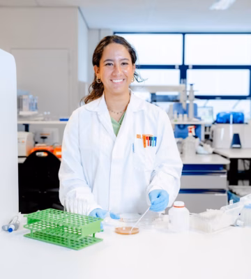 A person in a lab coat is working at a lab table with test tube racks and testing materials in a modern research environment.