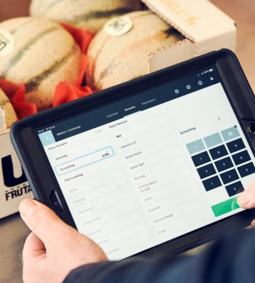 A tablet with inventory management software is used to check melons in a warehouse setting.
