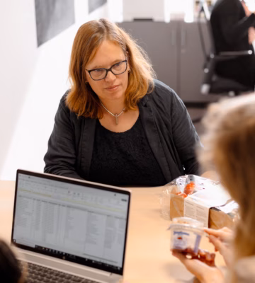 A meeting at a conference table where employees are working together using laptops and documents.