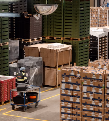 Magazijn met gestapelde pallets, kartonnen dozen en een autonome mobiele robot voor intern transport.