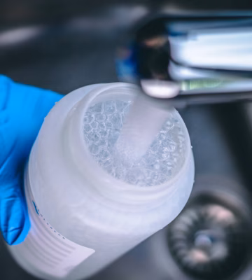 A person wearing blue sterile laboratory gloves is holding a flask while it is being filled with tap water.