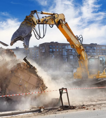Ein Bagger reißt ein Gebäude während der Abbrucharbeiten auf einer Baustelle ab, auf der viel Staub entsteht.