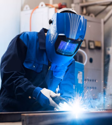 Ein Schweißspezialist führt MIG/MAG-Schweißarbeiten an einer Metallkonstruktion in einer industriellen Werkstatt durch.