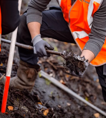 Mitarbeiter in orangefarbenen Sicherheitswesten sammeln bei Aufräumarbeiten auf einer Baustelle Abfall und Bodenreste ein.
