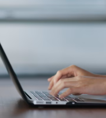 Hands typing on a laptop at a desk in a modern work environment