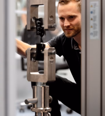 Eine Person überprüft während einer mechanischen Materialprüfung eine Zugversuchsanordnung in einer Universal-Materialprüfmaschine.