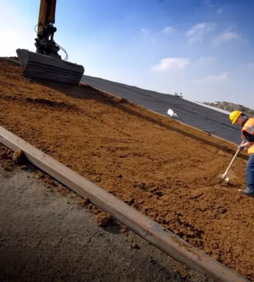 Schubversuch an Bodenmaterial während eines Straßenbauprojekts mit Bagger und manuellen Nivellierarbeiten.