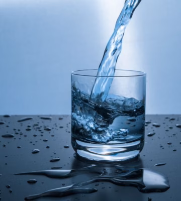 Water is being poured into a glass on a wet surface with visible water splashes.