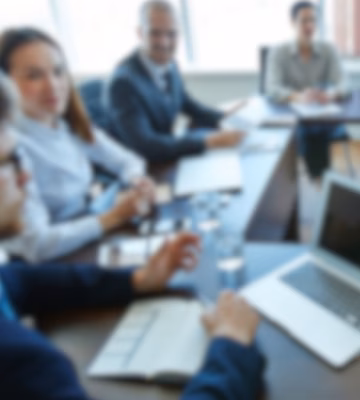Professionals nemen deel aan een overlegvergadering rond een vergadertafel met laptops en documenten, waarbij de nadruk ligt op bedrijfsadvies, strategische planning, betrokkenheid van belanghebbenden, projectmanagement en effectief teamwerk in een bedrijfsomgeving.