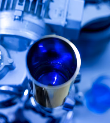 Close-up of a pharmaceutical manufacturing facility featuring a stainless steel tank containing a blue formulation, highlighting galenic development, drug formulation, and the precise production of pharmaceutical products in a controlled laboratory environment.