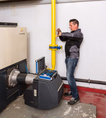 Technicus voert emissiemetingen uit aan een gasinstallatie met gele gasleiding, veiligheidsventiel en meetinstrument voor rookgas- en CO‑analyse.