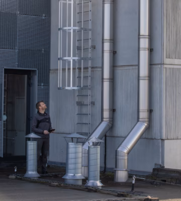 Technicus inspecteert industriële ventilatiekanalen en veiligheidsladder als onderdeel van CO‑covenant begeleiding en controle van luchtstromen en emissies.
