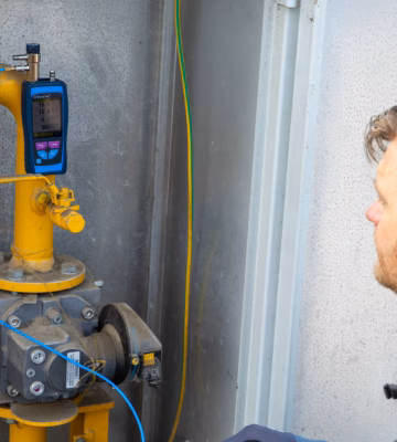Un technicien effectue une analyse des gaz de combustion à l'aide d'un appareil de mesure numérique raccordé à une conduite de gaz industrielle