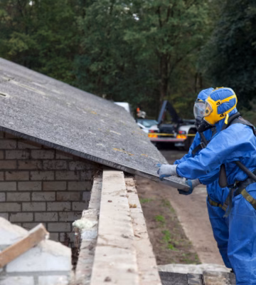 Twee medewerkers in volledige beschermingspakken voeren een asbestinspectie uit op een dakplaat in een buitenomgeving.