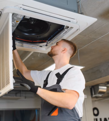 Un technicien inspecte et entretient un système de climatisation fixé au plafond.