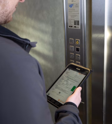 Un inspecteur contrôle une installation d'ascenseur et consigne ses constatations sous forme numérique pendant l'inspection.