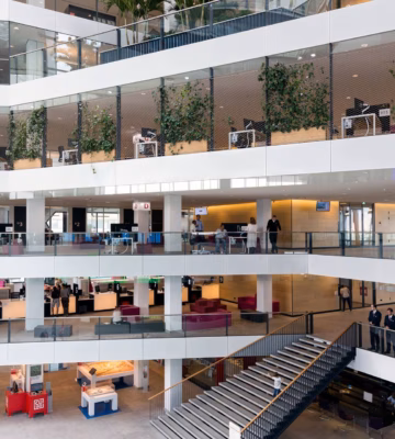Intérieur d'un immeuble de bureaux moderne avec des espaces de travail ouverts, plusieurs étages et des espaces verts intégrés.