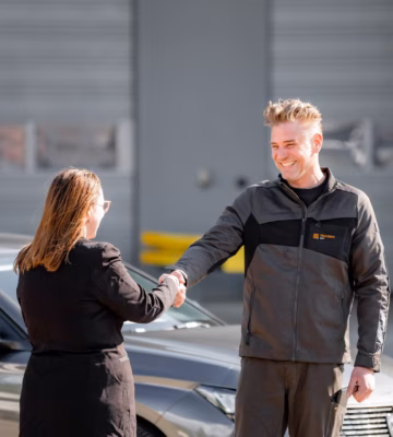 Deux personnes se saluent à côté d'une voiture dans un cadre d'inspection professionnelle.
