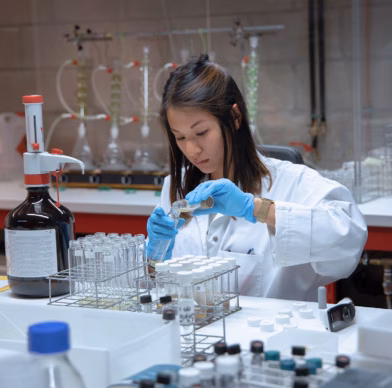 Een vrouw voert een test uit in een laboratorium. Ze draagt een laboratoriumjas en blauwe steriele laboratoriumhandschoenen en giet twee vloeistoffen bij elkaar.