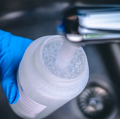 Iemand draagt blauwe steriele laboratoriumhandschoenen en houdt een fles vast terwijl deze met kraanwater wordt gevuld.