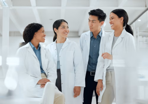 4 scientists in lab coats laughing in a laboratory