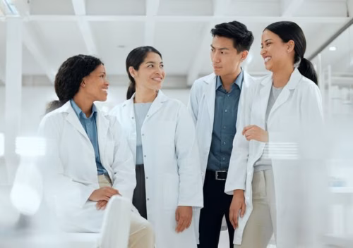 Four scientists in white lab coats smiling at each other.