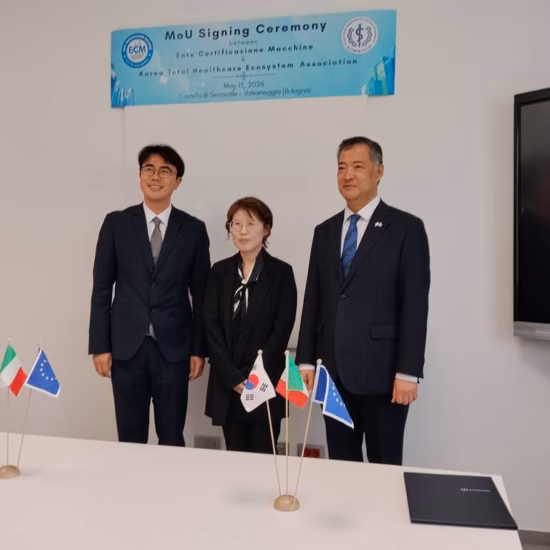Three participants are standing next to a table with small national flags during a formal international meeting.