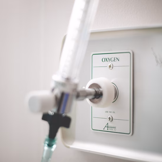 Close-up van een zuurstofaansluiting op medische apparatuur. Een transparante slang is verbonden met de aansluiting, die is gemarkeerd met de tekst "Oxygen". De afbeelding illustreert de toevoer van medische zuurstof binnen een zorg- of ziekenhuisomgeving.
