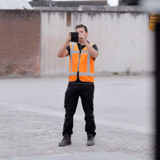 A surveyor is conducting a survey on a paved area using a handheld measuring instrument.