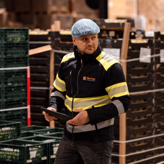 Un magasinier équipé d'une tablette contrôle les processus logistiques parmi des caisses en plastique empilées dans un centre de distribution.