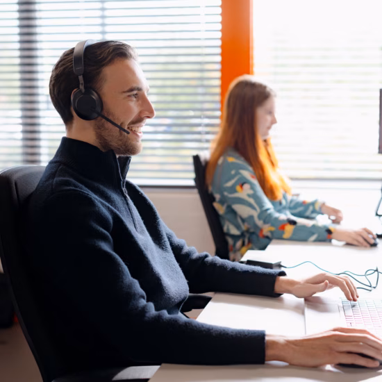 Customer service representatives are working with headsets and computers at their office desks.