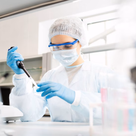Ein Laborant in steriler Schutzkleidung führt während einer Laboranalyse einen Pipettiervorgang durch.