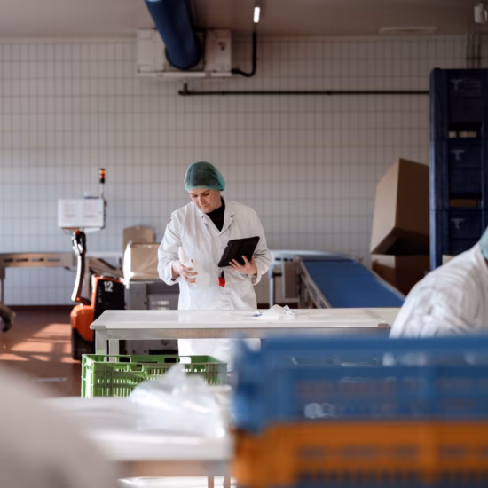 Employees perform quality control and processing in a food production area equipped with work tables and product crates.
