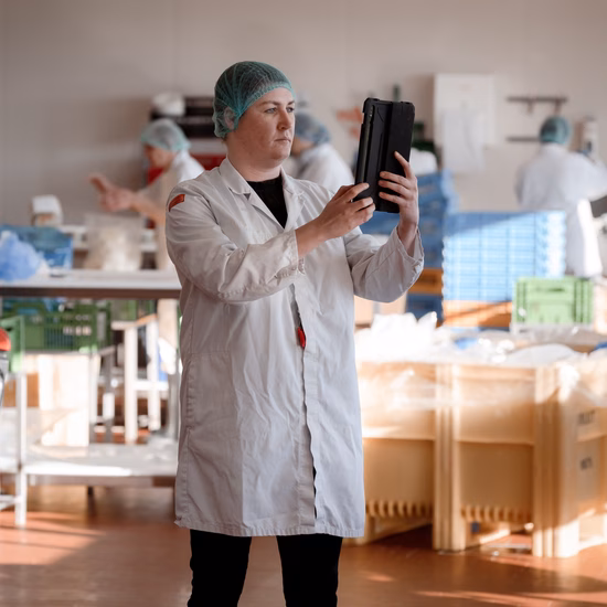 An employee in a white lab coat inspects black trays in a production environment for quality control.