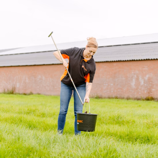 A person is taking a soil sample on grassland using a manual soil auger and a sample bucket.