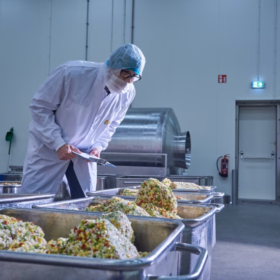 An employee wearing hygiene attire processes food products in a food processing production area.