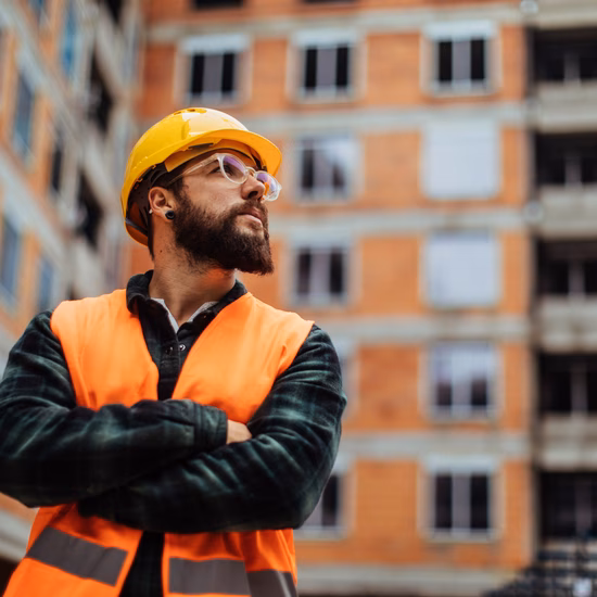 Ein Mitarbeiter mit Schutzhelm und reflektierender Sicherheitsweste inspiziert eine Baustelle für ein im Bau befindliches Gebäude.