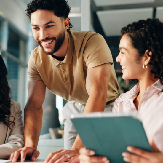 A group of colleagues are laughing and collaborating on a project in an office, with a tablet and a laptop, sharing ideas and enjoying teamwork.