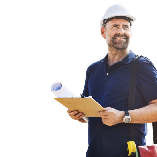 A man is standing on a construction site, wearing a safety helmet, holding a clipboard and a large rolled-up construction plan, looking around and smiling.