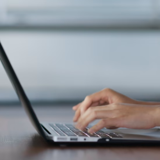 Hands typing on a laptop at a desk in a modern work environment
