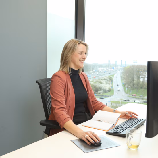 Frau, die während der Arbeit an ihrem Computer lacht, mit einem Notizbuch vor sich und einer Tasse Tee.