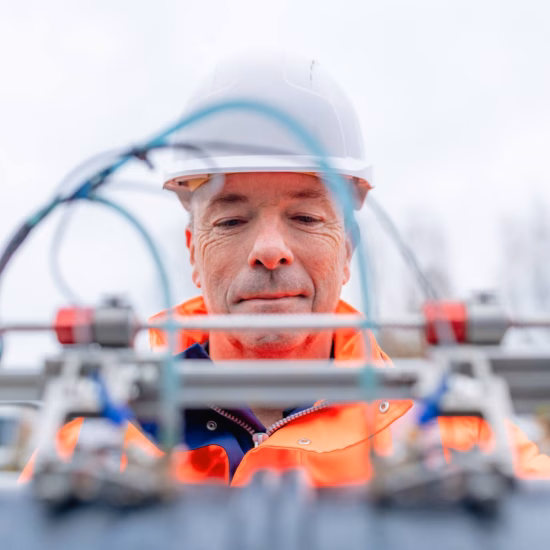 Inspector wearing an orange safety jacket and white helmet inspecting a large inspection pipe at an industrial work site.