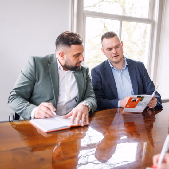 Two men discussing information from a brochure together during a meeting in an office space.
