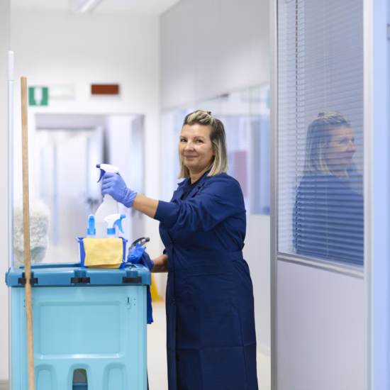 Woman smiling while cleaning a hallway inside a building.
